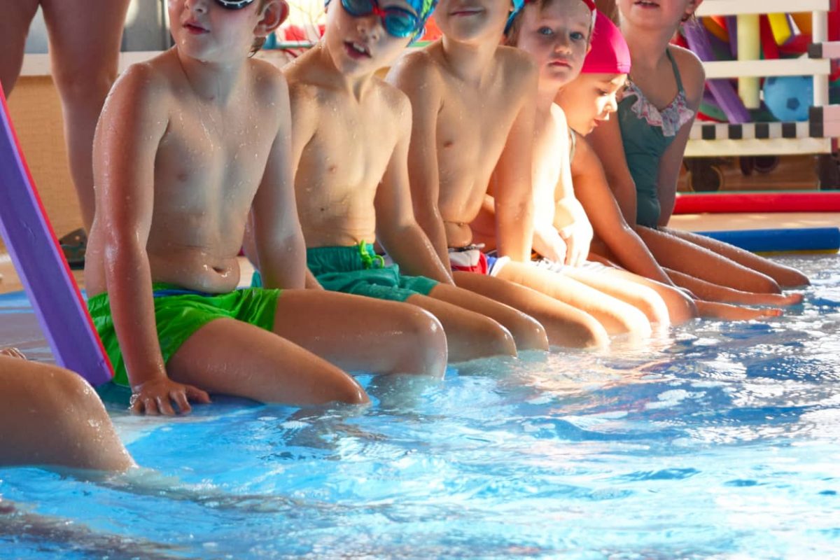 Alumnos de escuela de natación infantil sentados en la piscina