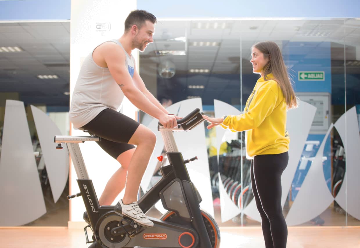 Monitora gimnasio con alumno en bicicleta de ciclo indoor
